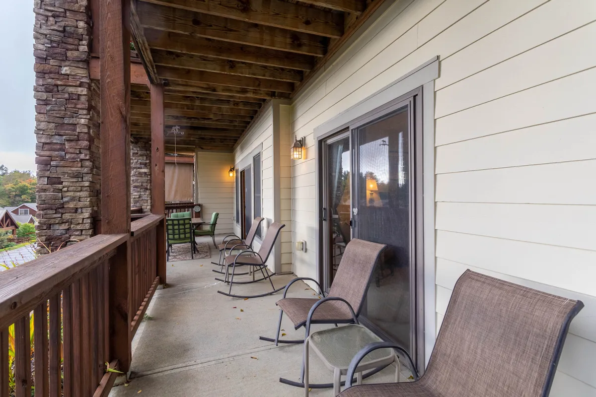 This image shows a tranquil exterior porch scene featuring sturdy rocky pillars, metal chairs arranged for conversation, and windows glowing with soft, inviting light. The setting evokes a sense of relaxation and leisure, perfect for unwinding after an adventurous day, with the porch positioned for sunset views and stargazing.