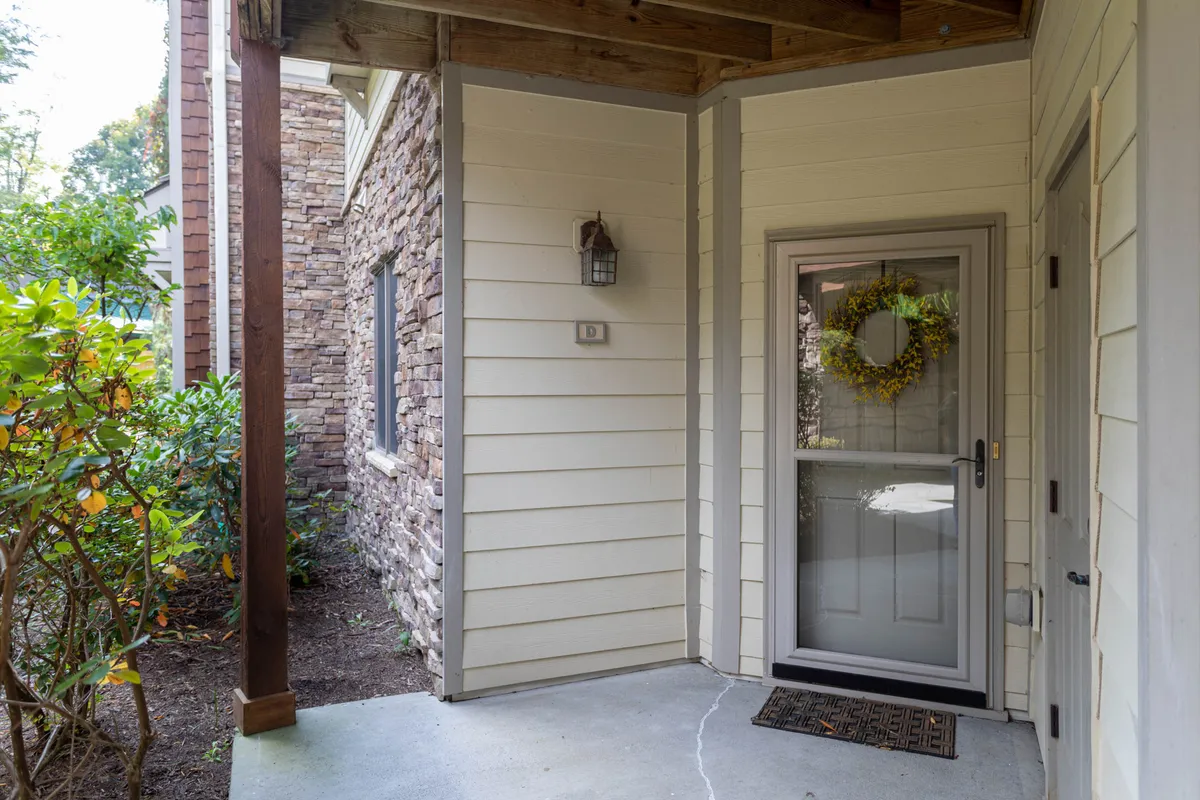 A close-up view of the front door area with a stone wall, decorative wreath, light fixture, and doormat. The space is tidy and welcoming, signaling high standards of cleanliness and a well-maintained entry.