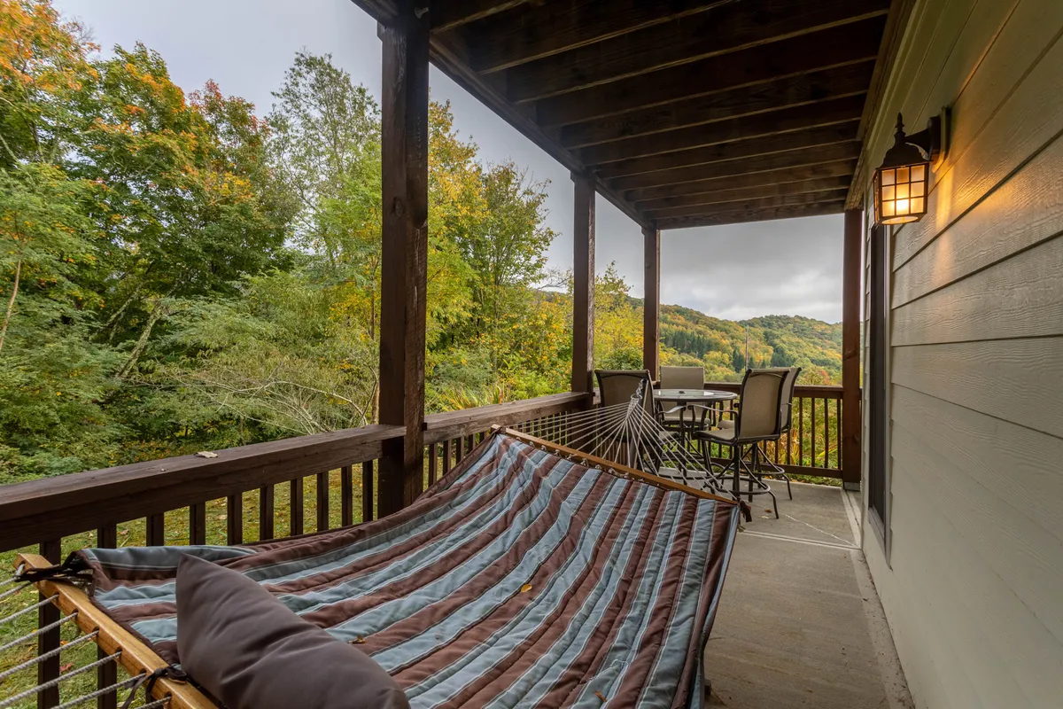 A tranquil outdoor space featuring a hammock and comfortable seating set amidst tall trees. The cozy setup invites relaxation, socializing, and immersion in nature, connecting guests to the outdoors and the changing seasons.