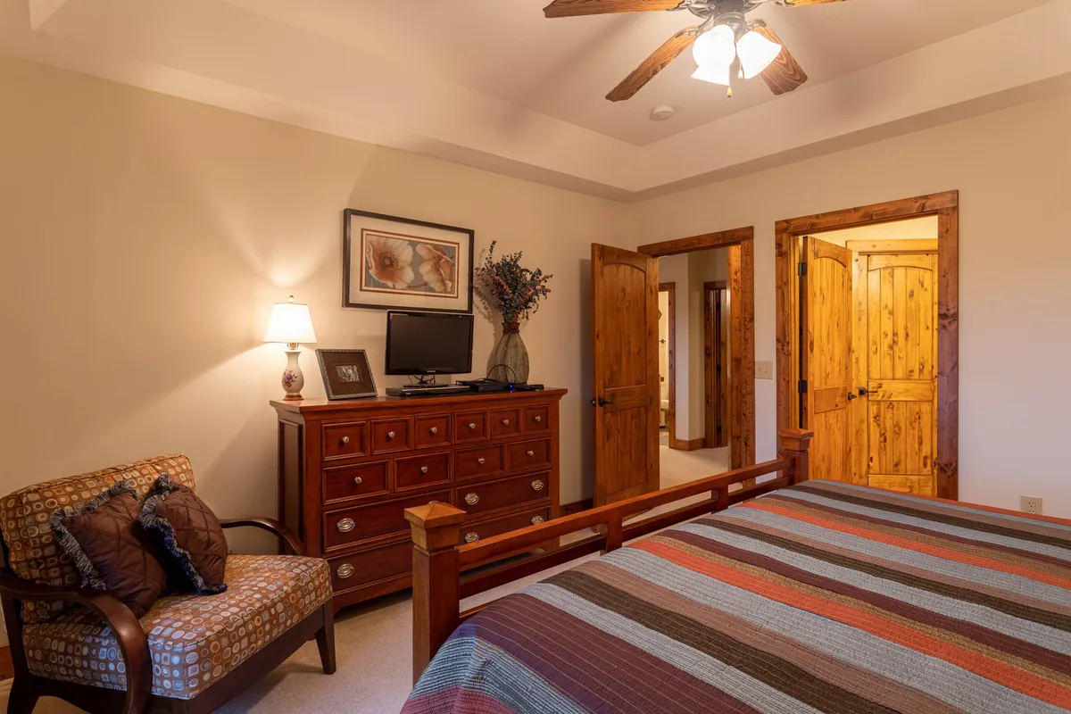 A cozy bedroom with a king bed adorned in colorful striped bedding, a wooden dresser, an inviting armchair, and a decorative lamp. Sunlight streams in, emphasizing the room's warmth and welcoming feel.