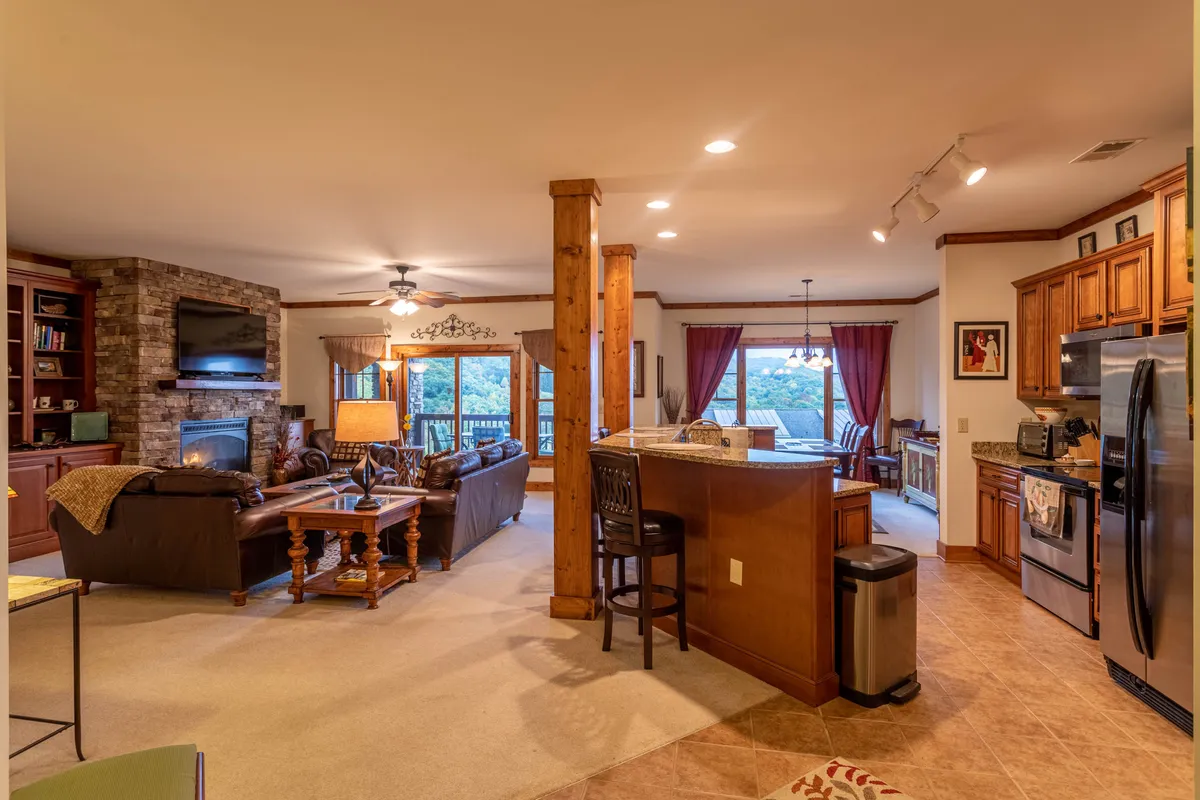 This open-concept room highlights a fireplace, a large kitchen island perfect for meal preparation or casual dining, comfortable seating, and large windows that bathe the space in natural light. The kitchen and living spaces flow seamlessly together.