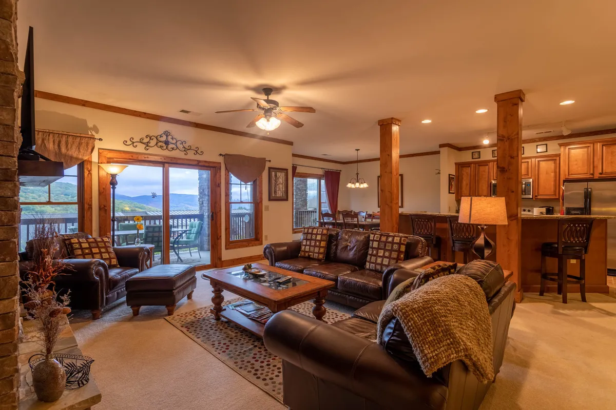 This interior shot features a leather sofa, wooden coffee table, large windows with scenic views, and a stone fireplace. The open layout allows natural light to fill the space, creating a warm, inviting environment ideal for relaxing after a day of exploration.