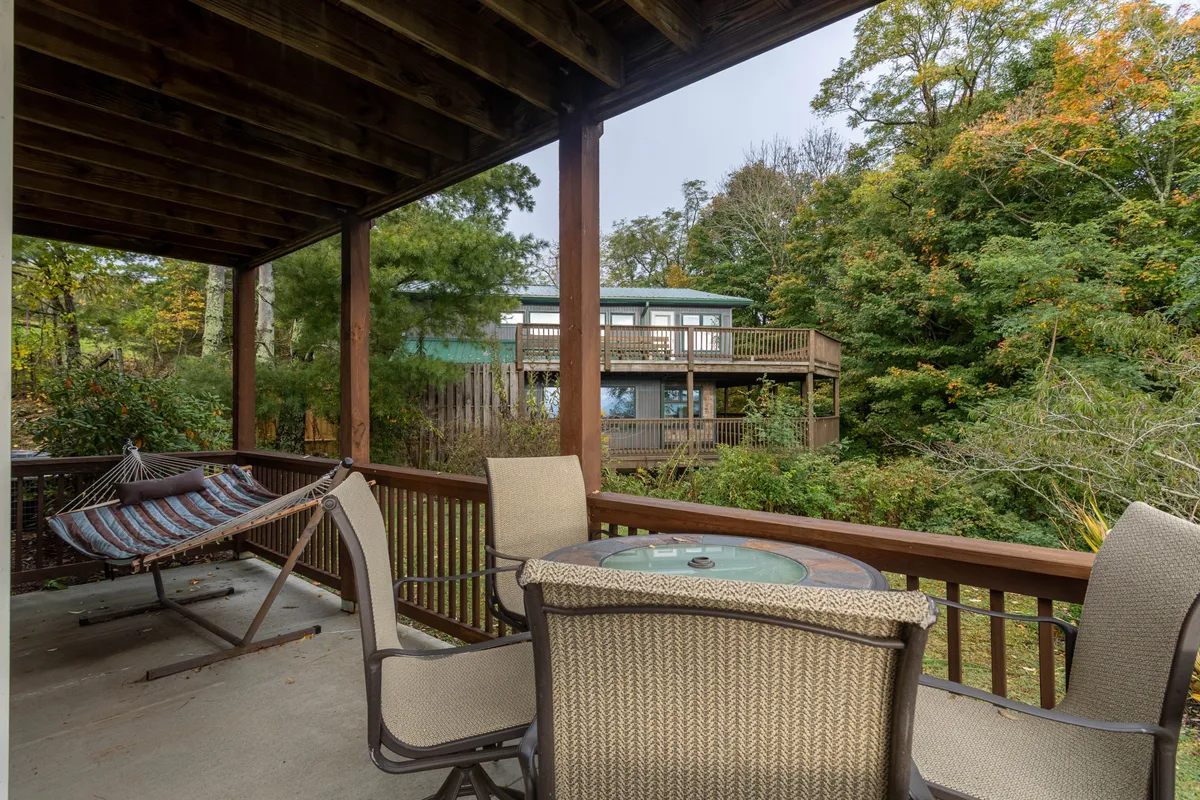 An outdoor living area, this image features a hammock and cozy seating space surrounded by lush greenery and a spacious deck structure. The natural atmosphere invites relaxation, morning coffee, and casual gatherings, enhancing the theme of winding down in style after a day out.