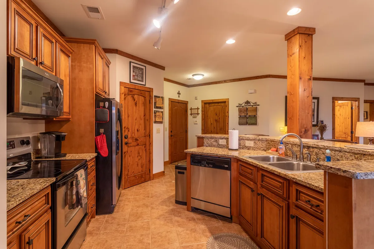 A spacious kitchen with granite countertops, wooden cabinetry, stainless steel appliances, and decorative wall art. The cabinetry suggests ample pantry space for storing supplies and groceries.