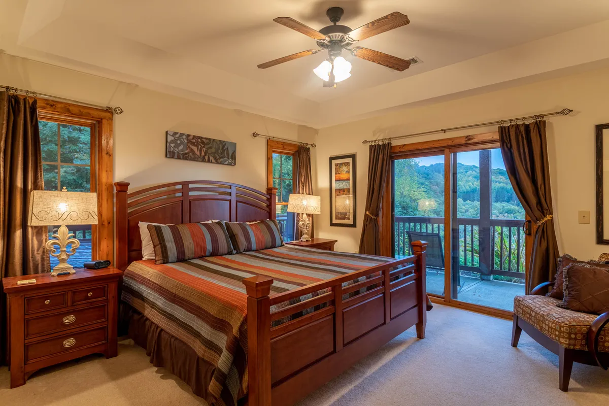A calm and inviting bedroom featuring a comfortable bed, soft lighting from bedside lamps, large windows that let in natural light, and a nightstand. The overall feel is restful and serene, perfect for a peaceful night's sleep.